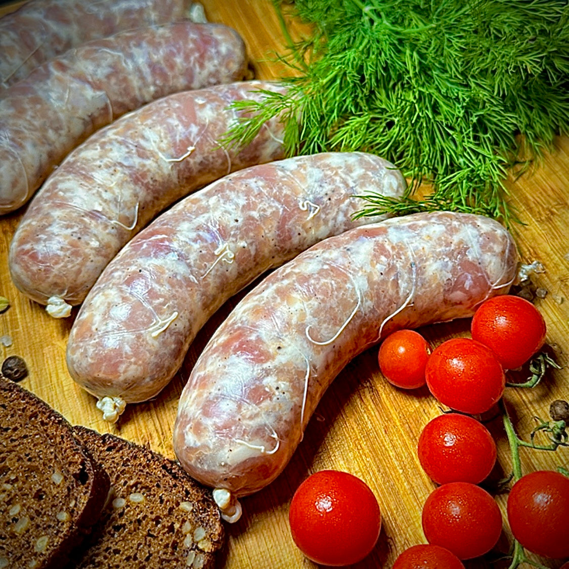 Fresh Pork Sausages for Grilling uncooked on rustic board with tomatoes and dill – Ukrainian Smokehouse