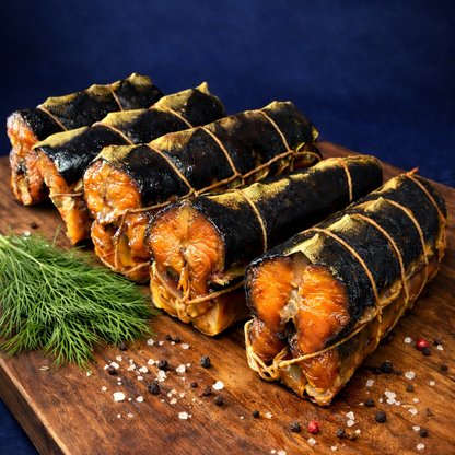 Row of smoked sturgeon roulades tied with twine on a wooden cutting board with dill and sea salt