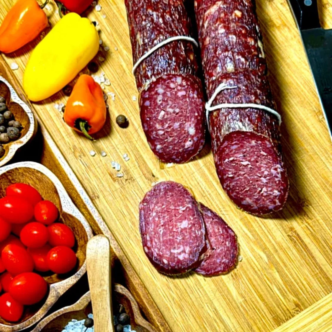 Dry-cured beef sausage sliced on a wooden board with vegetables and spices