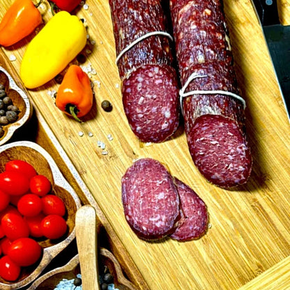 Dry-cured beef sausage sliced on a wooden board with vegetables and spices