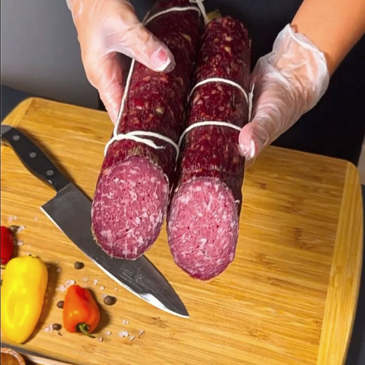 Dry-cured beef sausage held by hand over a wooden board with knife and spices