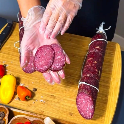 Sliced dry-cured beef sausage held in hand over a wooden board with whole sausage and spices